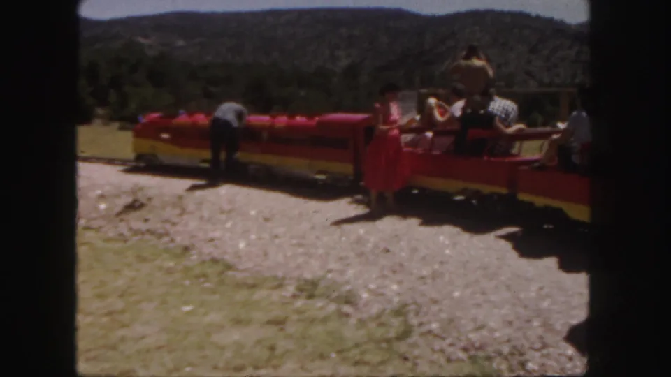 Colorado 1958 home-movie frame showing passengers near a red and yellow miniature train with hills in the background.