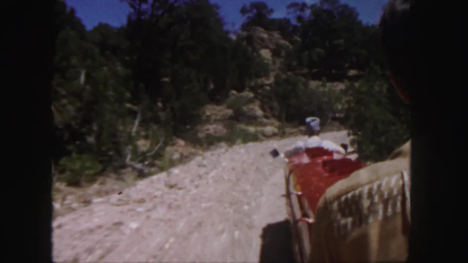 Moving 8mm view from the miniature train route, looking along a gravel path through trees and rocky terrain in Colorado.