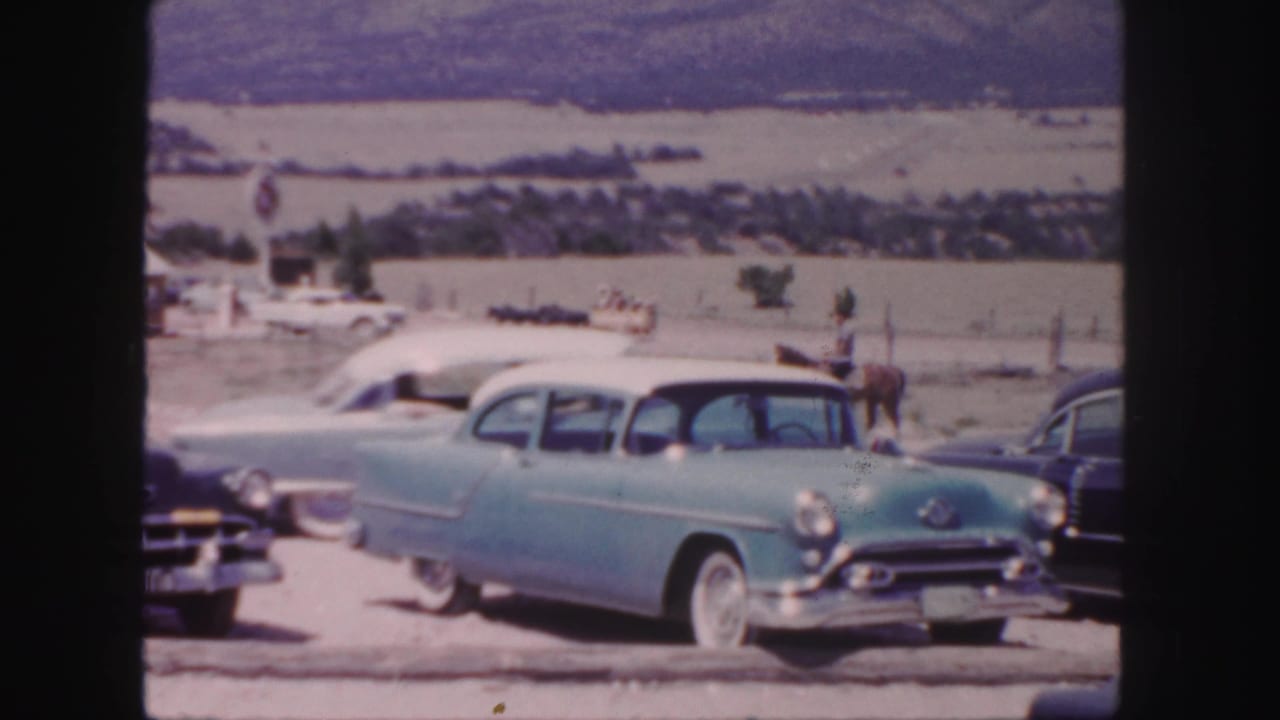 1958 Colorado 8mm frame showing a light blue sedan with white roof, nearby classic cars, open fields, and distant hills.