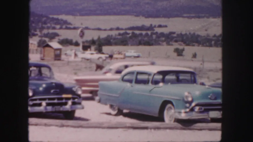 1958 Colorado roadside frame with classic cars in front and a horse rider crossing the open area behind them.
