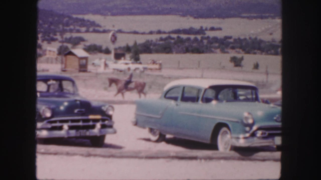 1958 Colorado 8mm frame showing mid-century cars near a horseback rider against open hills and distant buildings.