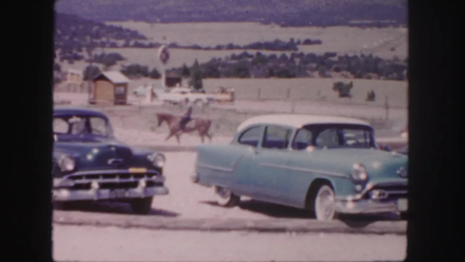 1958 Colorado 8mm frame showing mid-century cars near a horseback rider against open hills and distant buildings.