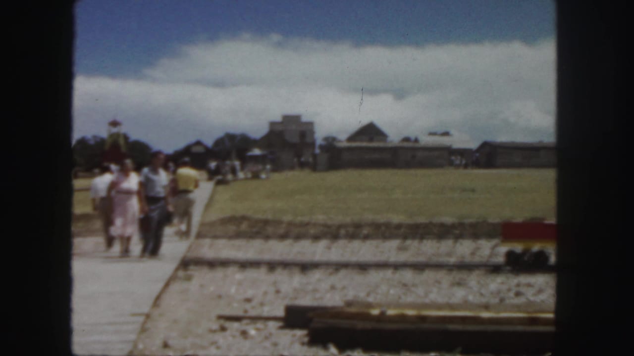 A small group of visitors walks on a path through a grassy area near rail tracks.