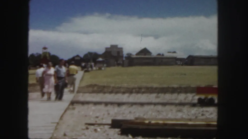 Adults in mid-century clothing walk through a rural Colorado attraction area beside a miniature rail line.