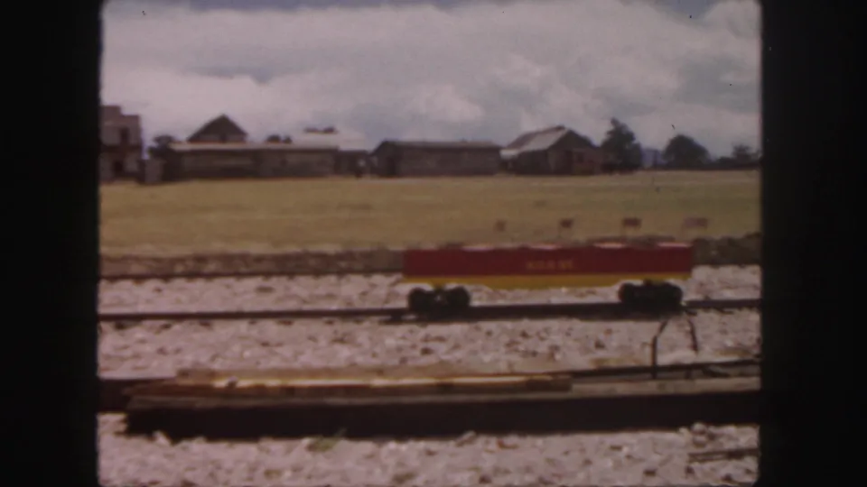 1958 Colorado home-movie frame of a red Wells Fargo rail car beside open grounds and rustic buildings under a cloudy sky.