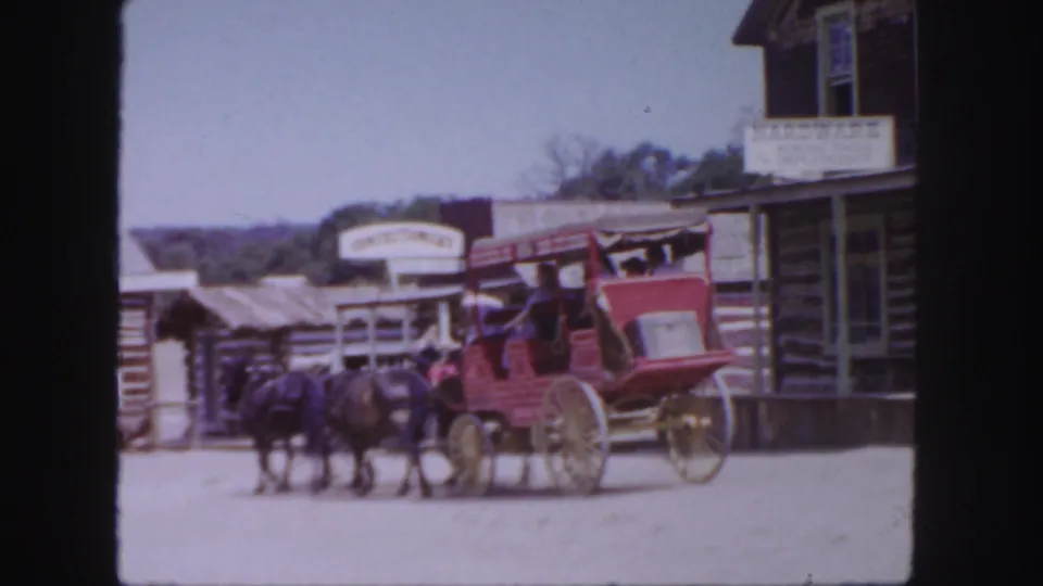 1958 Colorado frame showing a red stagecoach pulled by horses through a dusty Western-themed village street.
