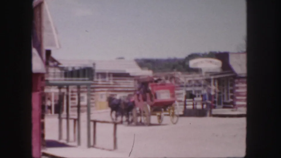 The red coach moves toward the edge of the 1958 Colorado frame, with horses, passengers, railings, and Western-style storefronts visible.