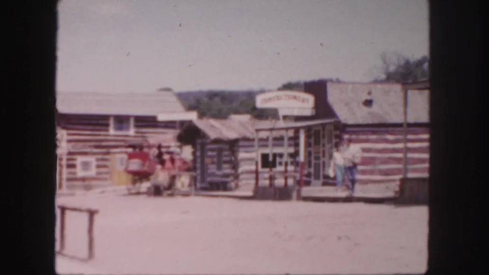 Western-style Colorado storefronts in 1958 with visitors near a red wagon and a readable confectionery sign above the entrance.