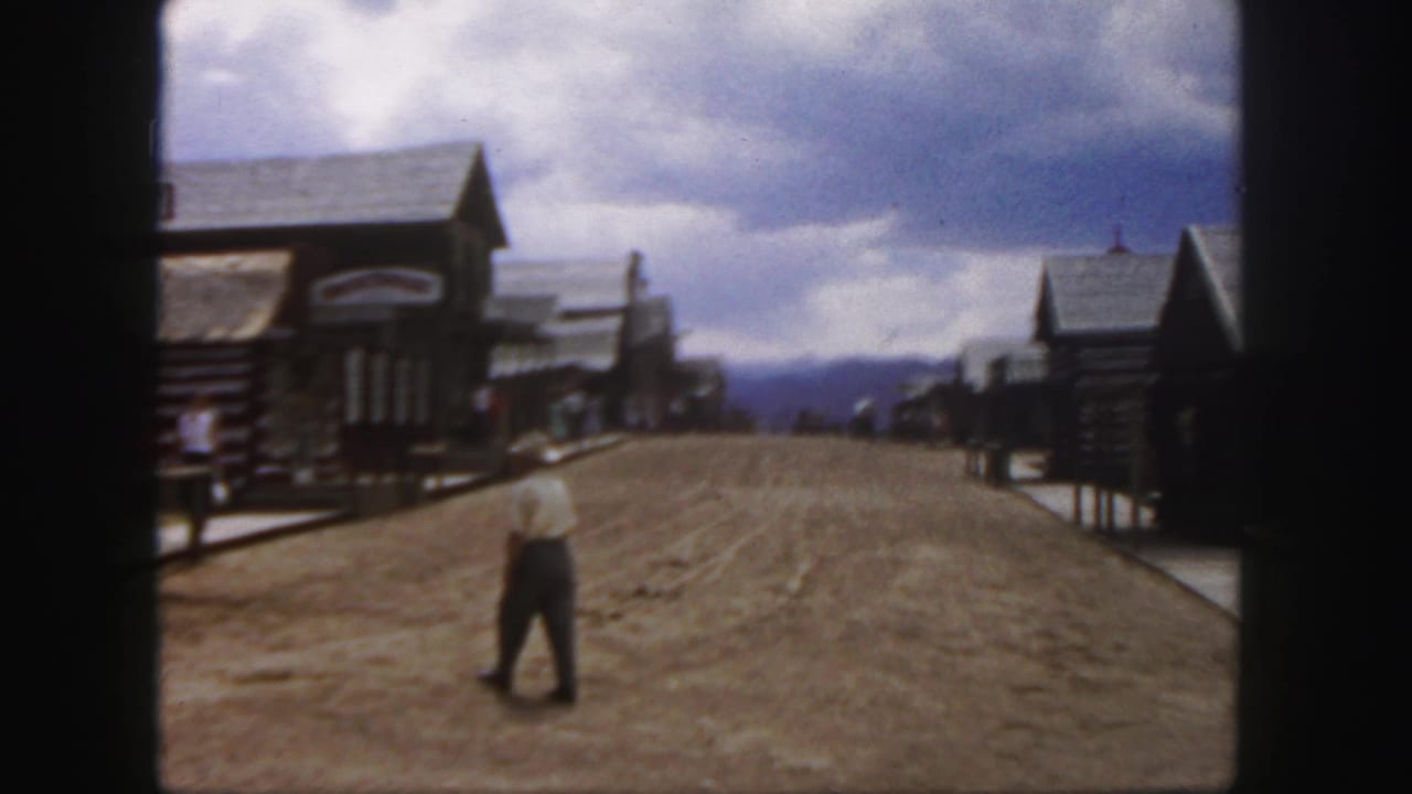 1958 Colorado home-movie frame showing a man in a light shirt and cowboy hat walking along an Old West-style dirt street.