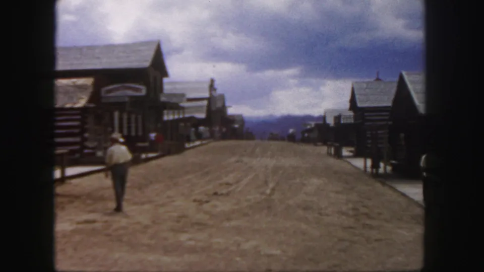 1958 Colorado home-movie view of a man walking away along a dusty Old West-style street with tourists in the distance.