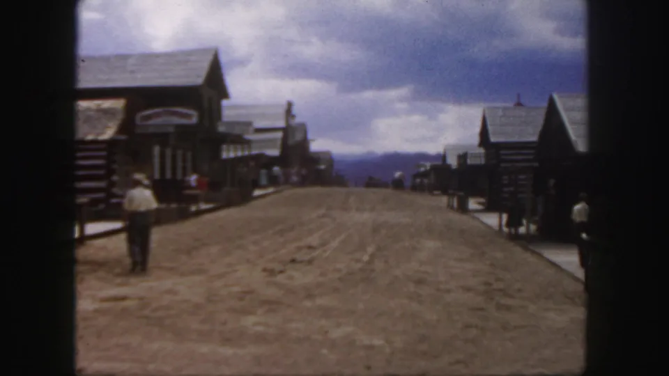 1958 Colorado frame showing the man near the left side of the Old West-style street as other visitors stand farther down the road.