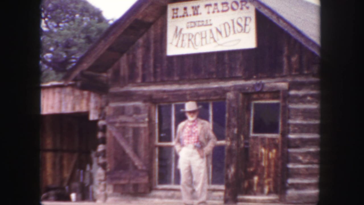 1958 Colorado 8mm frame showing a man posed outside a log storefront marked H.A.W. Tabor General Merchandise.