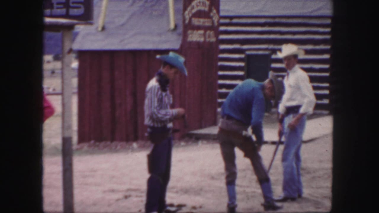 Three men in cowboy hats stand near a red wooden facade and log building in 1958 Colorado home-movie footage.