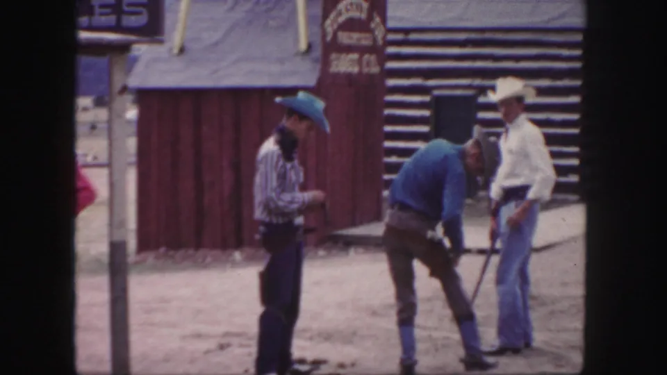 Three men in cowboy hats stand near a red wooden facade and log building in 1958 Colorado home-movie footage.