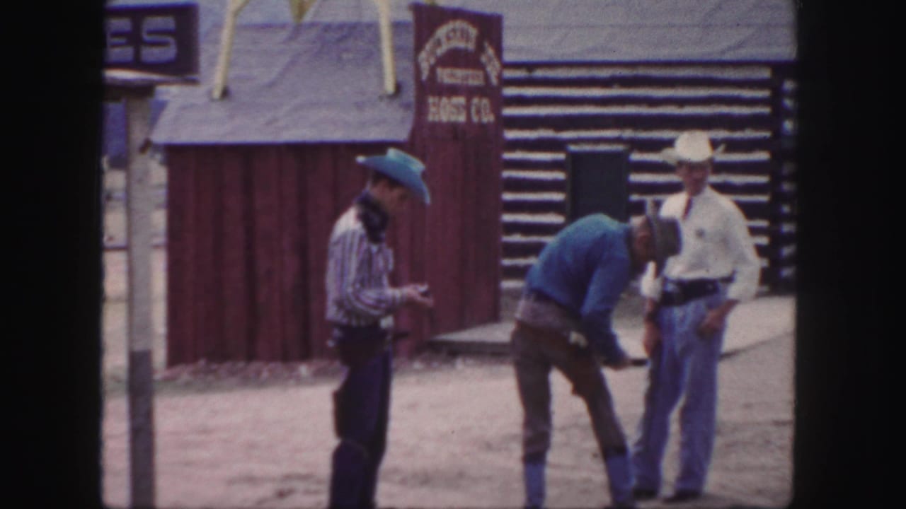 Two men stand while another bends forward near a Western-style building.