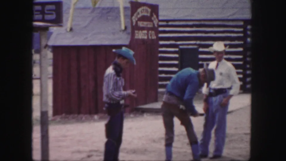 In a Colorado Western town setting, one cowboy-dressed man bends forward as two others stand nearby on a dusty street.