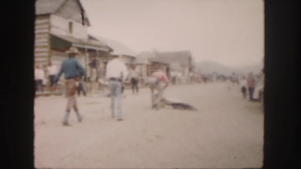 1958 Colorado 8mm frame showing men and onlookers on a dirt frontier-town street near an animal lying on the ground.