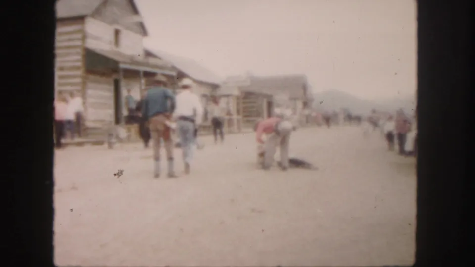 1958 Colorado home-movie frame with men in Western attire and bystanders around an animal on a dusty street.