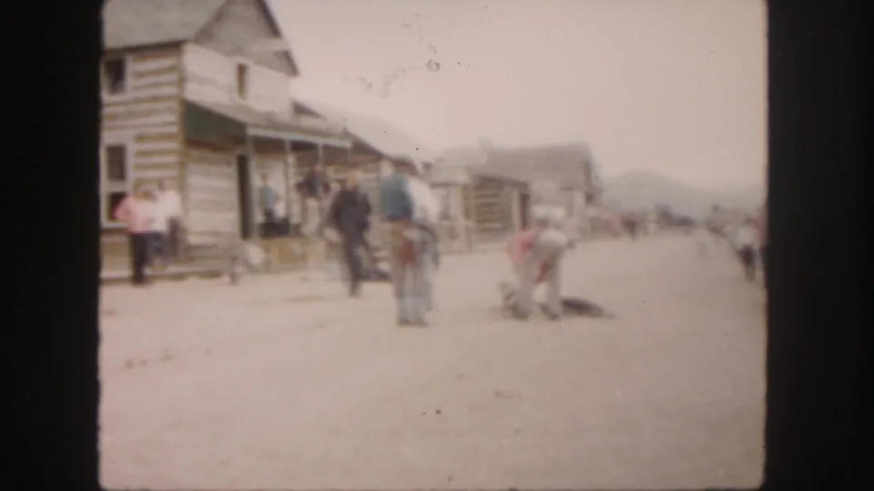 Soft 8mm frame from 1958 Colorado showing a frontier-style street with men, onlookers, and an animal on the ground.