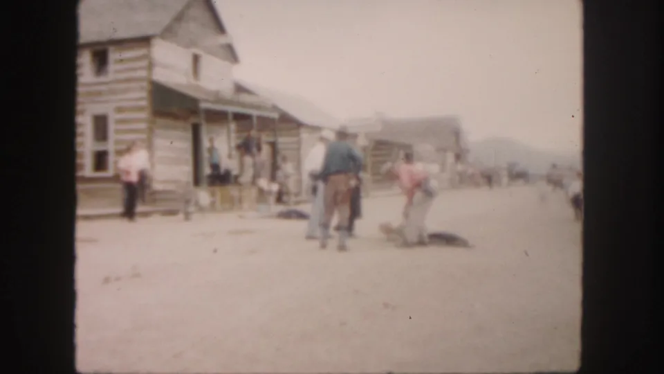 1958 Colorado 8mm frame with log storefronts, cowboy-hatted men, and an animal on a dirt street.
