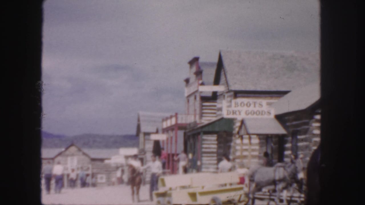 Western-style street with log storefronts, horses, wagon, visitors, and BOOTS DRY GOODS sign.