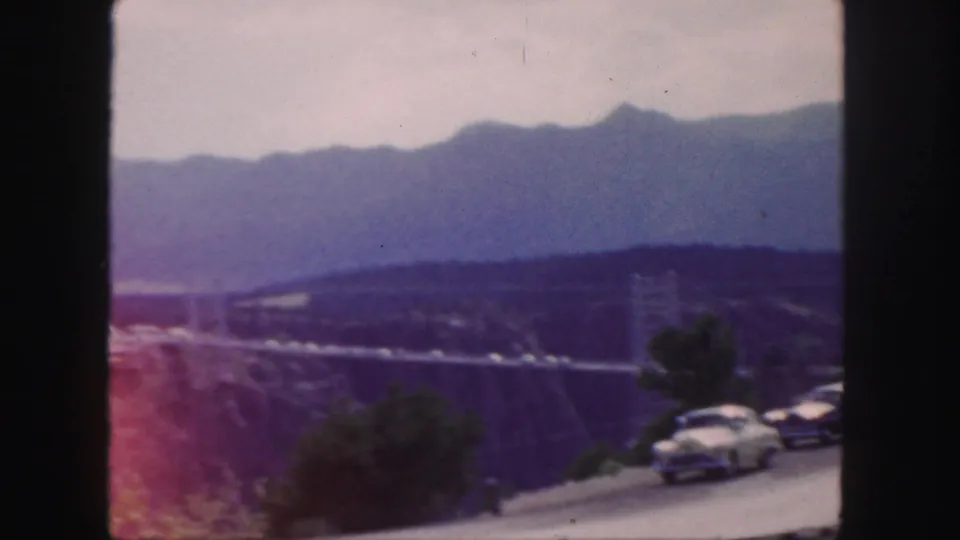 Colorado roadside overlook with parked cars, a bridge across the valley, and hazy mountain ridges beyond.