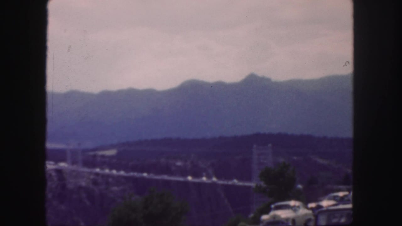 Suspension bridge across a canyon with cars and mountains in the background.