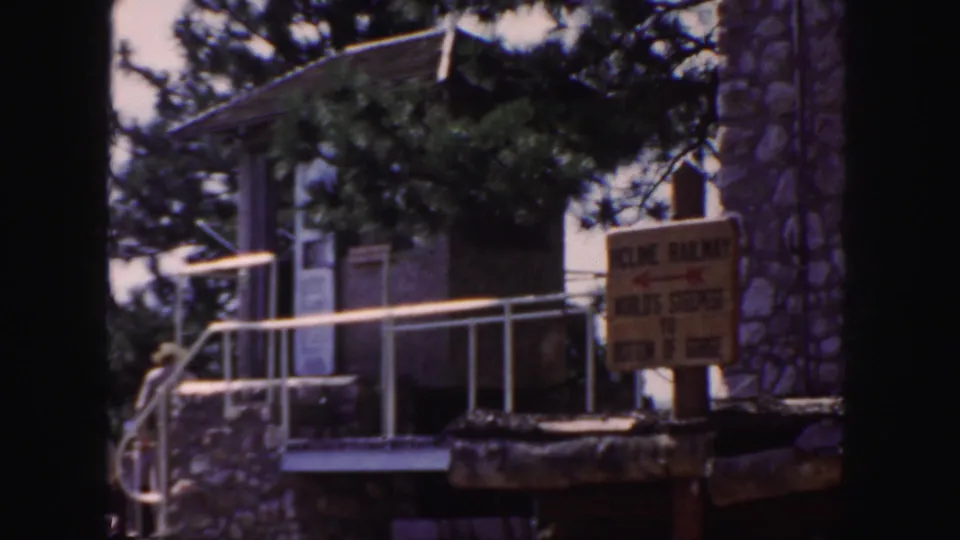 1958 Colorado tourist-overlook frame showing a small building, railings, trees, stonework, and a readable sign mentioning the world's steepest gorge.