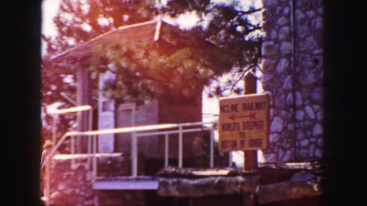 Yellow attraction sign in front of stone building with trees and railing.