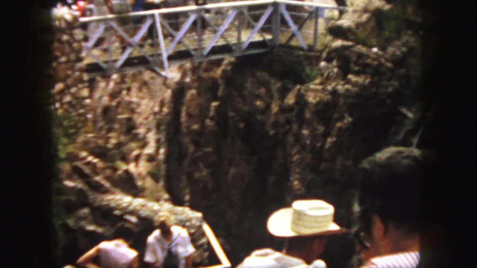 1958 Colorado canyon overlook scene with tourists below a metal walkway, rocky gorge walls, and foreground visitors partly visible.