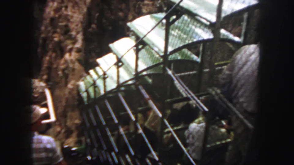 The rail bus passes close to the camera, showing its side structure, roof, and passengers against the Colorado canyon backdrop.