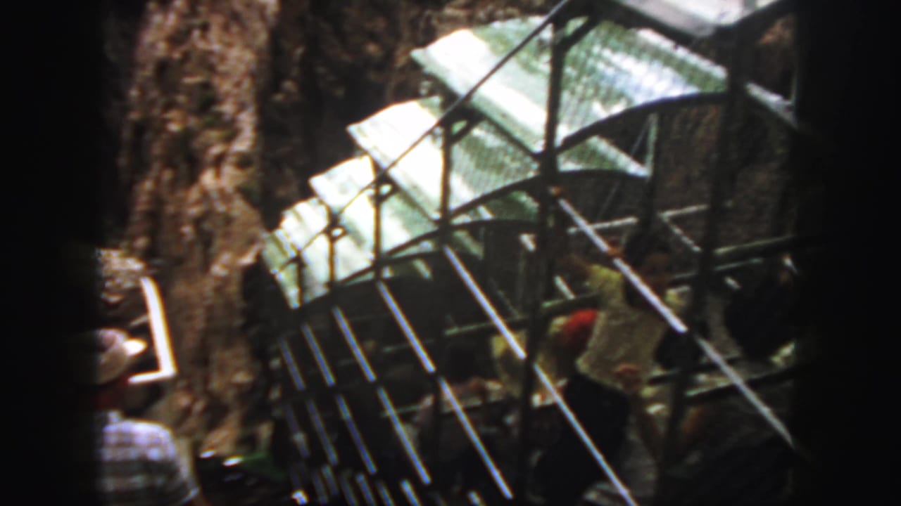 Passengers and metal-framed gondola structure beside a steep rock wall.