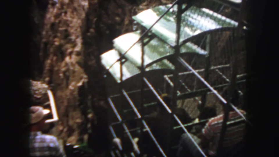 A Colorado mountain shuttle or gondola structure appears close to a rock wall, with passengers partly visible inside or nearby.