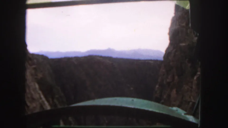 From inside the mountain shuttle, the camera looks past a curved green edge toward distant Colorado ridges and pale sky.
