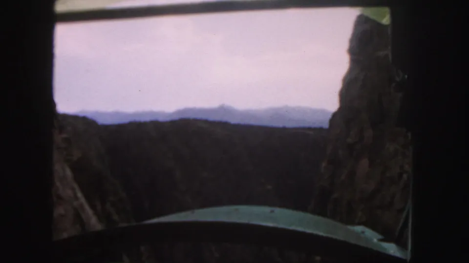 The 8mm frame looks from the shuttle toward layered mountain ridges, with rock and a curved green foreground edge visible.