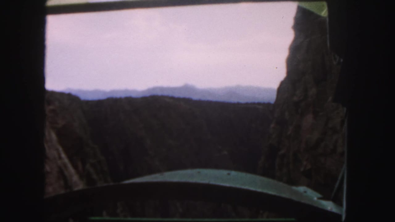 1958 Colorado 8mm frame showing a canyon and rocky cliffs through a vehicle window during a mountain pass descent.