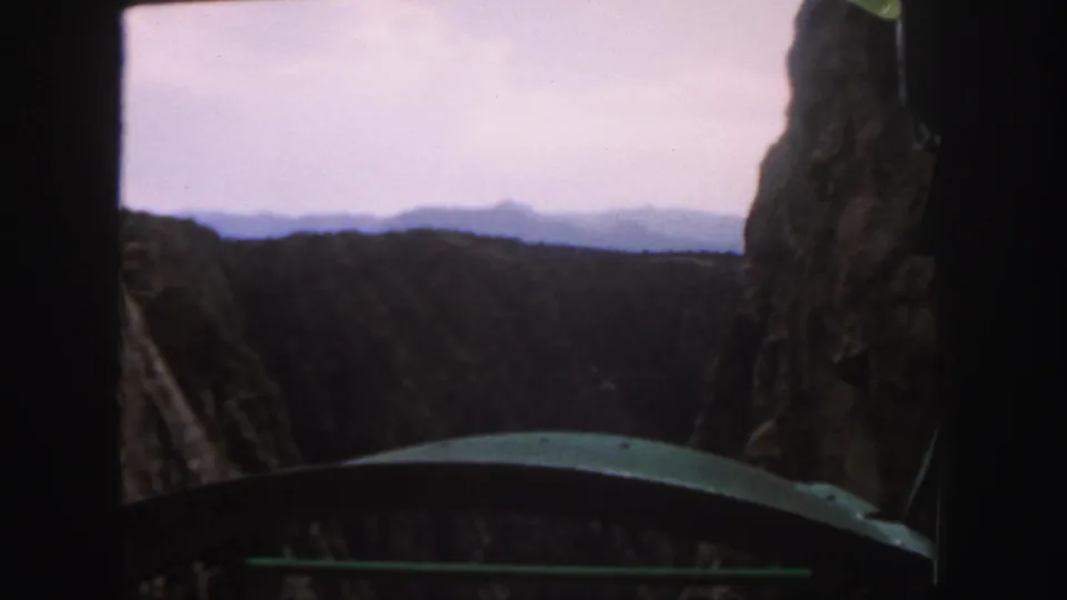 1958 Colorado travel footage frame with steep rock walls and distant mountains viewed from inside a moving vehicle.