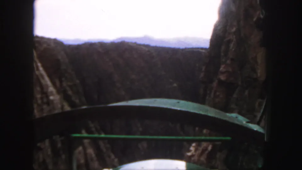 1958 Colorado mountain-pass frame with cliffs on both sides and distant terrain beyond the vehicle window.