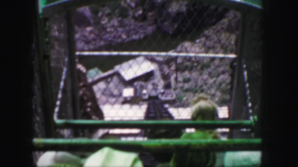 Colorado mountain ride footage shows the track below through the green car frame and safety fencing, with rocky terrain beyond.