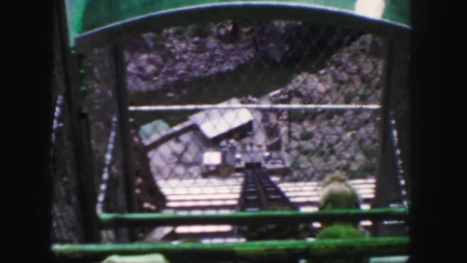 The final frame holds the Colorado mountain descent view, with green railings, chain-link fencing, a track, and rocky terrain below.
