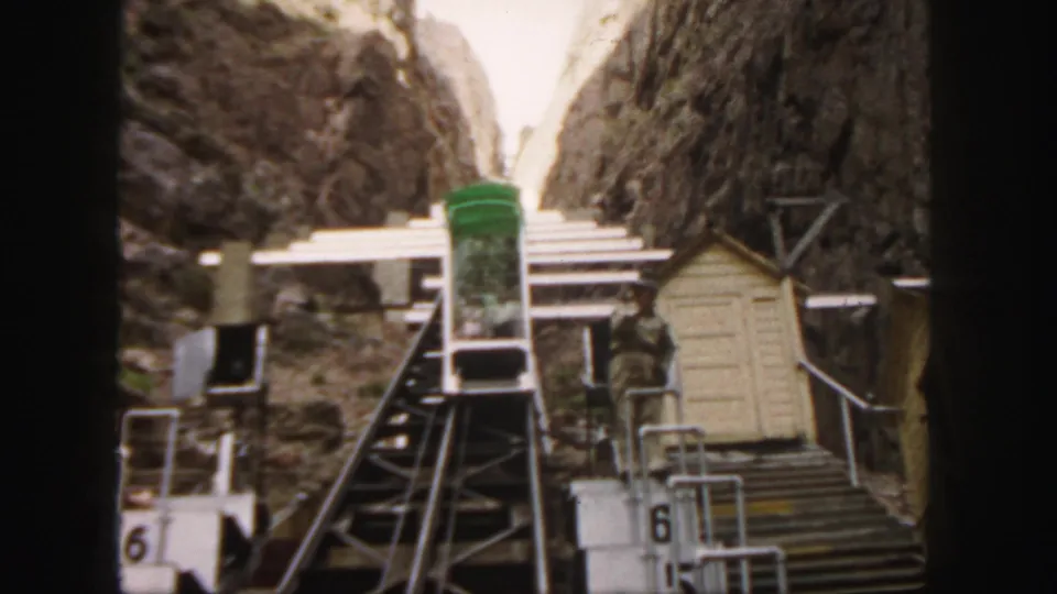 1958 Colorado footage frame with a green funicular car at a mountain station and a person standing near the platform.