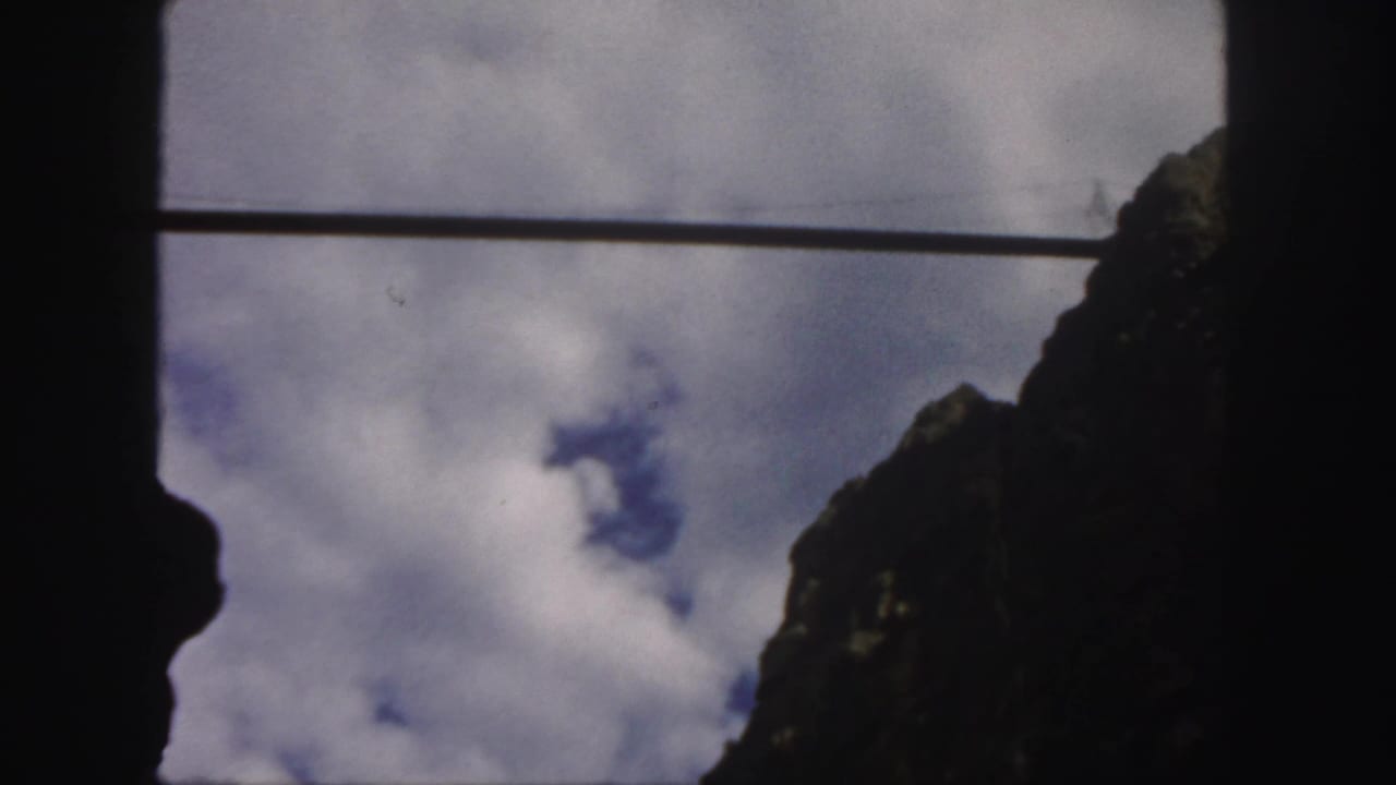 Cloudy blue sky seen past a dark frame and rocky slope.
