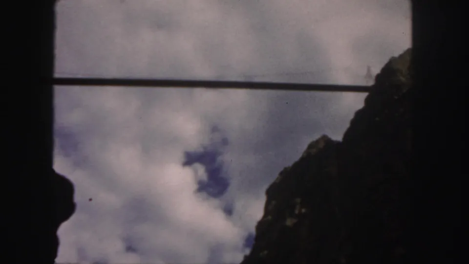 1958 Colorado 8mm still with a rugged rock silhouette, drifting clouds, blue sky, and a dark horizontal bar across the frame.