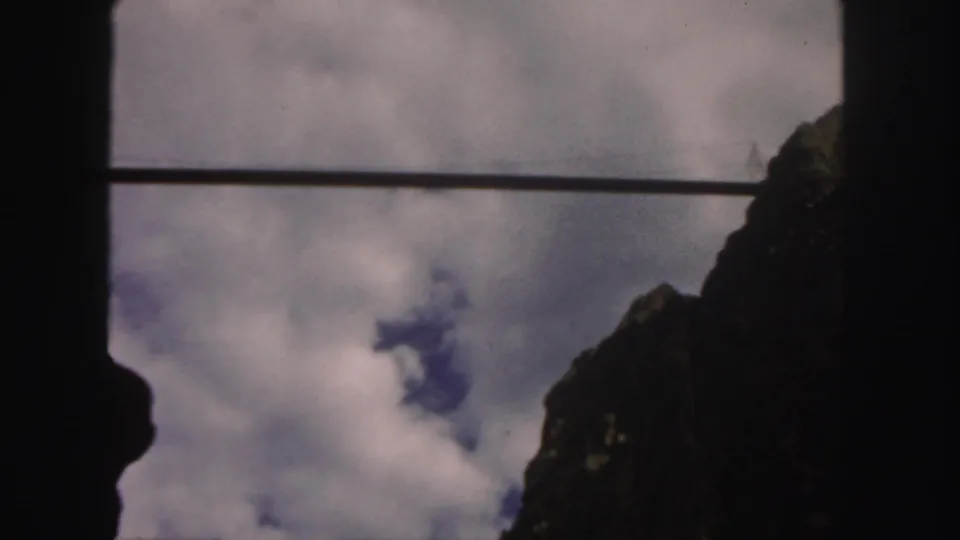 1958 Colorado 8mm frame showing a cloud-filled sky, a dark rocky slope, and silhouetted framing around the view.