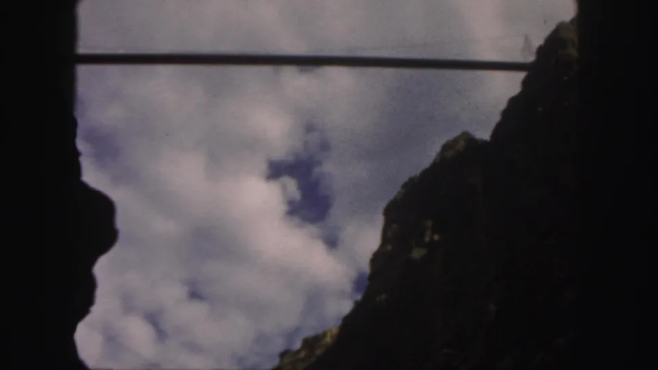 A 1958 Colorado home-movie view shows pale clouds drifting between shadowed mountain walls with blue sky visible beyond.