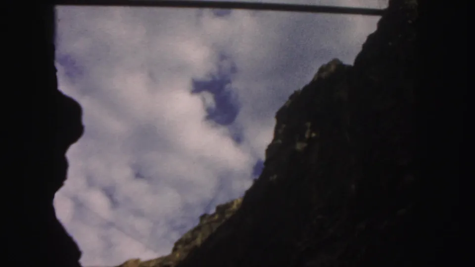 A tight 1958 Colorado 8mm composition frames clouds and blue sky between dark, rugged mountain slopes.