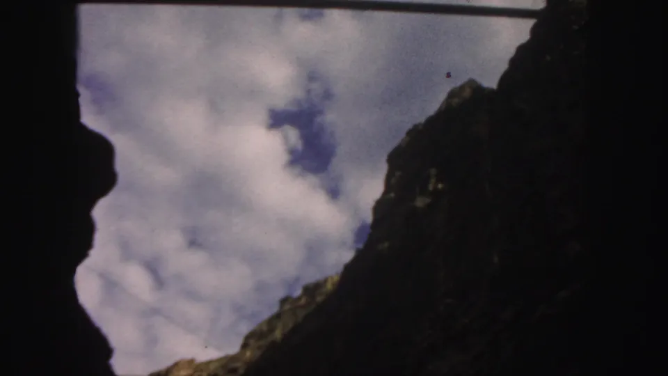 1958 Colorado 8mm frame looking past a dark foreground edge toward clouds above a steep rocky cliff.