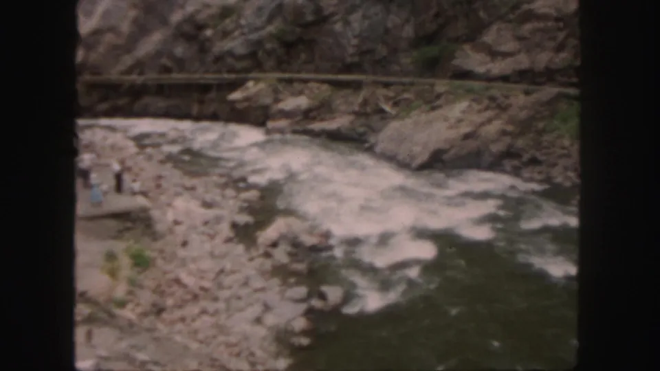 1958 Colorado home-movie view of a fast river in a rocky gorge with distant people standing near the water.