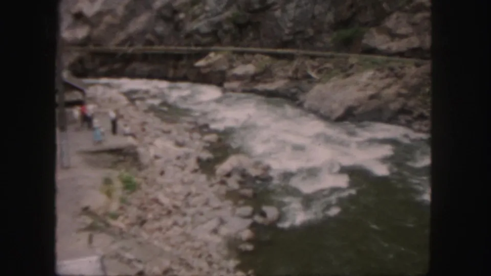 1958 Colorado 8mm footage shows visitors beside a rocky riverbank as whitewater rushes through the gorge.