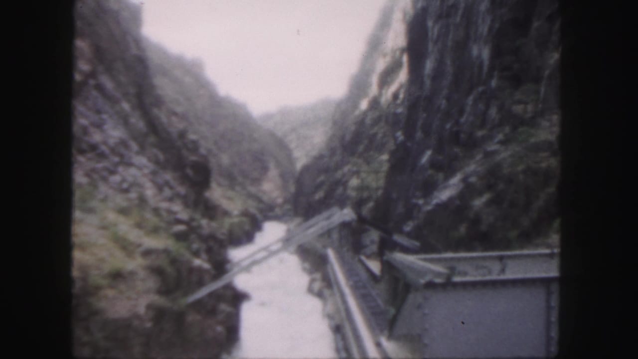 1958 Colorado 8mm frame looking down a steep rocky canyon from a wooden bridge, with a narrow river below.